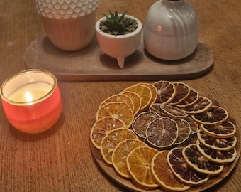May include: A wooden tray with a red candle, a small potted succulent, and a white ceramic vase. The tray is surrounded by dried orange and lime slices.