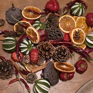 Peut inclure: Un assortiment d'éléments décoratifs comprenant des tranches d'orange séchées, des pommes de pin, des piments rouges et des sphères rayées vertes et blanches. L'arrangement est disposé sur une surface en bois, créant une esthétique rustique et naturelle.
