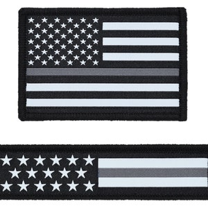 May include: Two black and white American flag patches with a thin gray stripe across the middle. The top patch is a standard size flag, while the bottom patch is a thin rectangular shape.