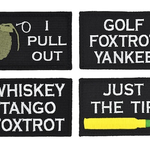 May include: Four black fabric patches with white text. The top left patch has a green grenade with a pin and the text "I PULL OUT". The top right patch has the text "GOLF FOXTRT YANKEE". The bottom left patch has the text "WHISKEY TANGO FOXTRT". The bottom right patch has a yellow bullet with a green tip and the text "JUST THE TIP".
