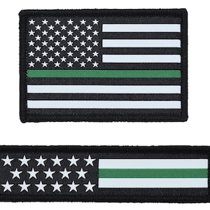 May include: Two black and white American flag patches with a green stripe. One patch is rectangular with stars and stripes, the other is a horizontal rectangle with stars and stripes.
