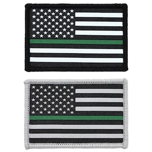 May include: Two embroidered patches featuring an American flag with a green stripe across the middle. The top patch has a black background and the bottom patch has a gray background.