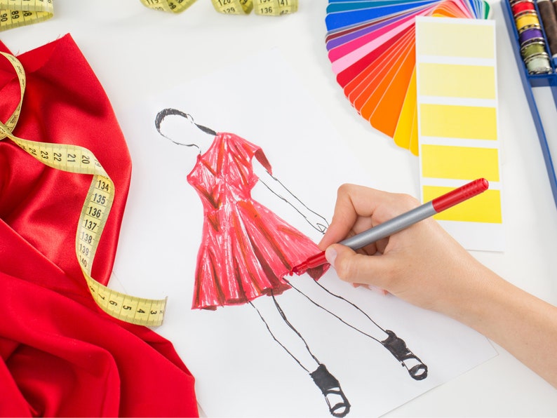 May include: A fashion designer sketches a red dress on white paper using a red marker. A yellow measuring tape, red fabric, and a color palette are also visible.