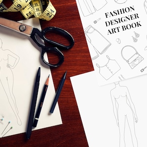 May include: A fashion designer art book with a white background and black line drawings of clothing, accessories, and a fashion figure. The book cover has the text "Fashion Designer Art Book" in black.