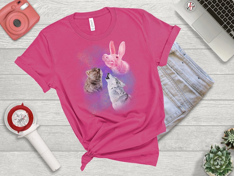 May include: Pink t-shirt with a graphic of a pink pig, a wolf, and a cat singing. The graphic is surrounded by a purple and blue nebula-like background.