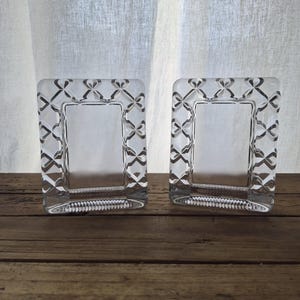 May include: Two rectangular clear glass picture frames featuring a repeating diamond and cross-hatch pattern along the thick borders. The frames have a smooth, polished finish with a clear center opening for displaying photographs or small art prints.