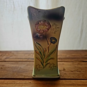 May include: A vintage ceramic vase with a light green, brown, and gold floral design. The vase has a square shape with rounded edges and a wide opening.