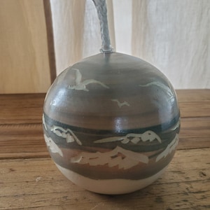 May include: A ceramic oil lamp with a white wick and a brown, white, and gray design of birds flying over mountains and water.