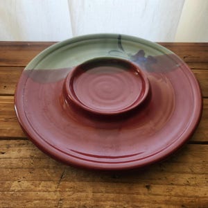 May include: A red and green ceramic serving dish with a smaller, round dish in the center. The dish is perfect for serving snacks or dips.