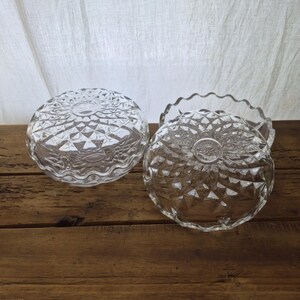 May include: Two clear glass dishes with a faceted diamond pattern and scalloped edges. The dishes are round with a textured surface that reflects light, featuring a central circular design on the base and a wavy rim around the perimeter.