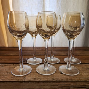 May include: Six clear glass wine glasses with a textured surface. The glasses are arranged in a row on a wooden surface.