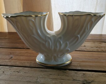 Könnte beinhalten: Eine weiße Keramikvase mit goldener Verzierung. Die Vase hat ein einzigartiges Design mit zwei Ausgüssen und ein strukturiertes Blumenmuster.