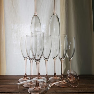May include: A set of nine champagne glasses with pink rims. The glasses are arranged in a pyramid shape on a wooden surface.