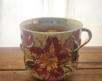 Taza de café de porcelana antigua con flor rosa y detalles dorados.