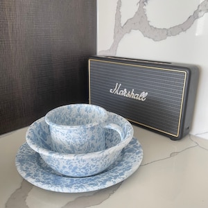 May include: A blue and white speckled enamelware dish set with a matching mug and a black Marshall speaker with gold trim. The speaker has the word "Marshall" in white script.