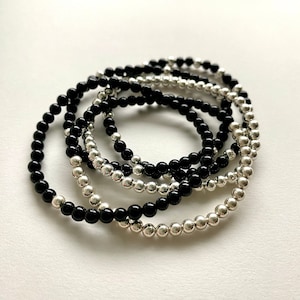 May include: A set of black and silver beaded bracelets. The bracelets are stacked on top of each other, creating a layered look.