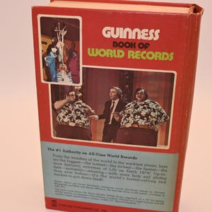 May include: A vintage Guinness Book of World Records, featuring a red cover with the title in white and green. The book showcases images of record-breaking feats and individuals, with text describing the book's content.