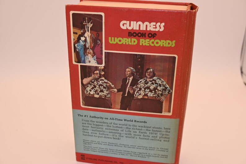May include: A vintage Guinness Book of World Records, featuring a red cover with the title in white and green. The book showcases images of record-breaking feats and individuals, with text describing the book's content.