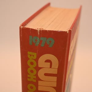 May include: A vintage book with a red cover, featuring the year "1979" in green. The title "BOOK OF" is visible in large, yellow letters. The book's pages are a light beige color.