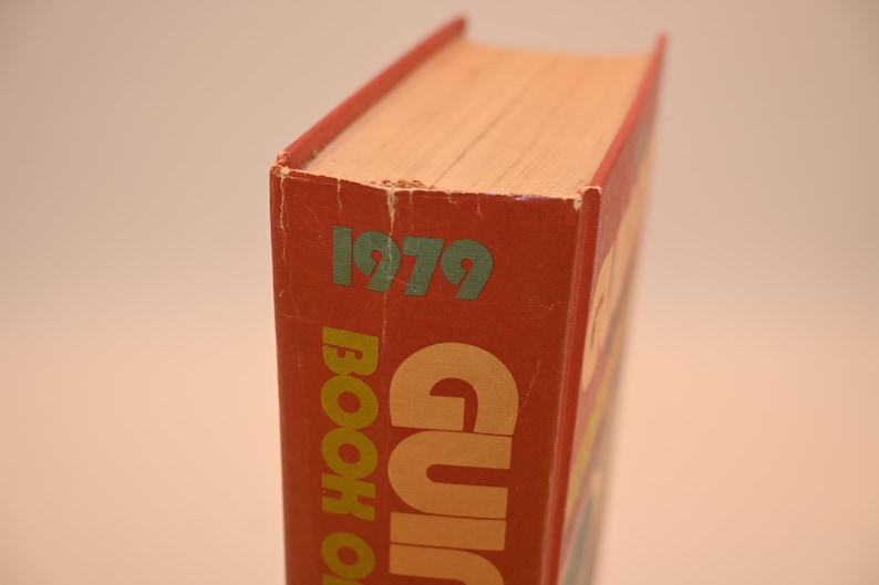 May include: A vintage book with a red cover, featuring the year "1979" in green. The title "BOOK OF" is visible in large, yellow letters. The book's pages are a light beige color.