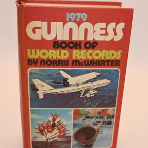 May include: A vintage 1979 Guinness Book of World Records. The red cover features the title in large white and yellow letters, with images of an airplane, a group of people, and a wooden horn. The book is by Norris McWhirter.