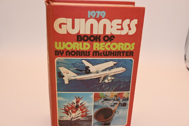 May include: A vintage 1979 Guinness Book of World Records. The red cover features the title in large white and yellow letters, with images of an airplane, a group of people, and a wooden horn. The book is by Norris McWhirter.