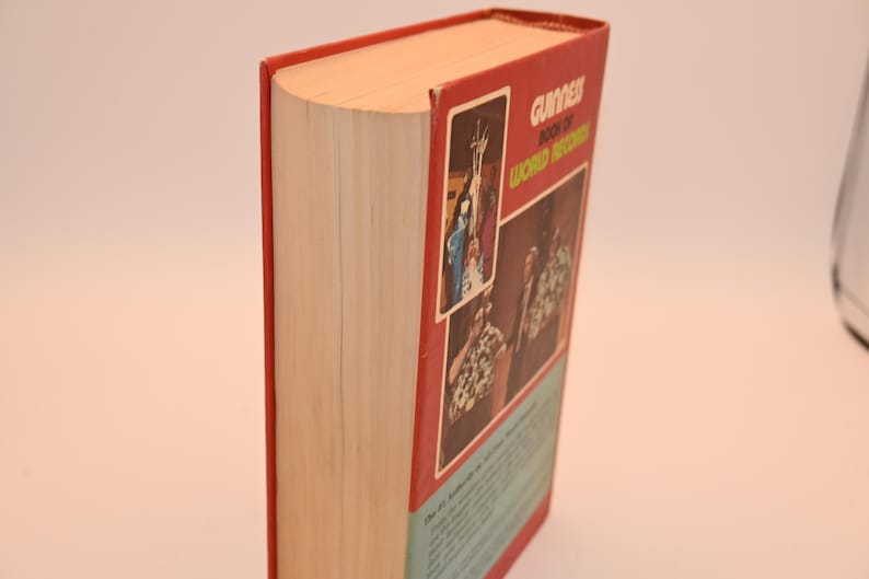 May include: A hardcover book titled "Guinness Book of World Records" with a red cover and spine. The book's pages are visible, and the cover features images and text. The book is set against a neutral background.