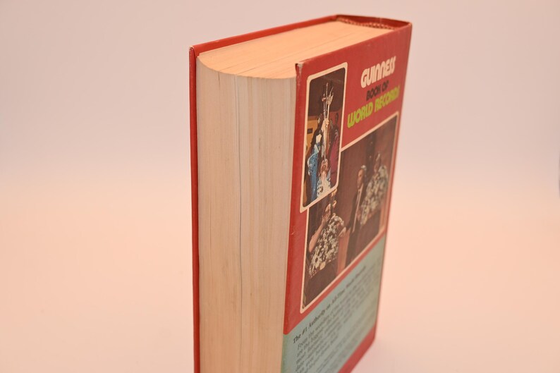 May include: A hardcover book with a red cover and the title "Guinness Book of World Records." The book's spine is visible, showing the pages and the red cover. The cover features images and text.