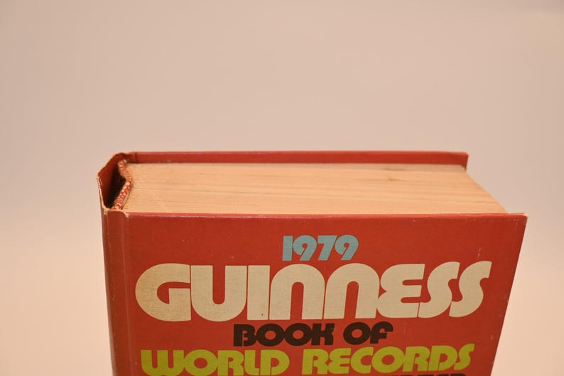 May include: A vintage 1979 Guinness Book of World Records. The book has a red cover with white and yellow lettering. The book's pages are a light tan color. The book is in good condition, with some wear and tear on the edges.