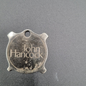 May include: A silver-colored metal key chain with a round tag that says "John Hancock" in a black font.