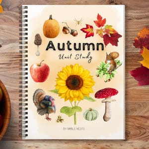 May include: A spiral-bound notebook with the title "Autumn Unit Study" and illustrations of fall elements like a pumpkin, apple, sunflower, and squirrel. The notebook is on a wooden surface with a bowl of apples.