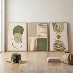 Peut inclure: Trois impressions d'art abstraites encadrées. Les impressions présentent des tons terreux de vert, beige et marron. L'une a des formes superposées, une autre des rayures et des carrés, et la troisième un soleil et des feuilles. Les cadres sont en bois clair.