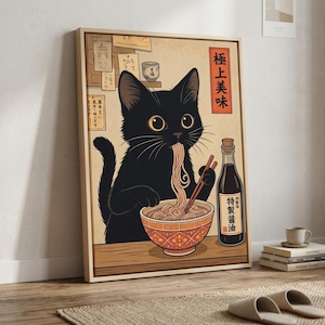 Könnte beinhalten: Gerahmter Kunstdruck mit einer schwarzen Katze, die Ramen-Nudeln isst. Die Katze hat große gelbe Augen und benutzt Essstäbchen. Eine Flasche Sojasauce und eine Schüssel Nudeln sind ebenfalls zu sehen. Japanischer Text ist vorhanden.