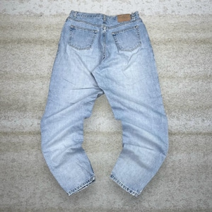 Puede incluir: Vaqueros de mezclilla azul claro con un diseño clásico de cinco bolsillos. Los vaqueros tienen un lavado descolorido y un corte de pierna recta. La parte trasera presenta dos bolsillos y un parche de cuero. Los vaqueros están planos sobre una superficie neutra.