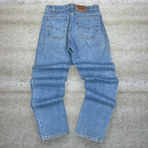 May include: Light blue denim jeans with a classic five-pocket design. The jeans feature a brown leather patch on the back waistband and a faded wash. The jeans are laid flat on a neutral surface.