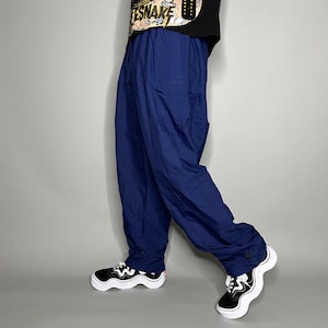 May include: Navy blue athletic pants with a relaxed fit. The pants have a drawstring waist and a small Nike logo. The person is wearing black and white sneakers with a wavy design.