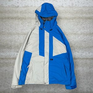 May include: A blue, white, and gray hooded winter jacket. The jacket features a color-block design with a blue hood and sleeves, a white and gray body, and the brand name "VOLCOM" printed on the front.