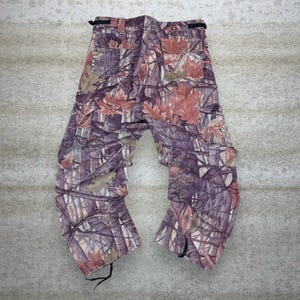 May include: A pair of camouflage cargo pants featuring a pattern of purple, brown, and tan foliage. The pants have multiple pockets, a button closure, and drawstrings at the ankles. The overall design is a blend of natural elements.