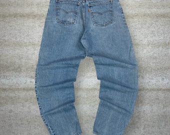 Puede incluir: Vaqueros de mezclilla azul claro con un estilo clásico de cinco bolsillos. Los vaqueros presentan un lavado descolorido, un parche de cuero en la cintura trasera y la etiqueta icónica de la marca Levi's. Los bolsillos traseros tienen las costuras arqueadas características.