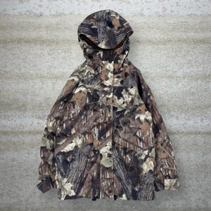Puede incluir: Chaqueta con capucha de camuflaje en tonos marrón, verde y beige, diseñada para integrarse en un entorno forestal. La chaqueta cuenta con cremallera completa, múltiples bolsillos y capucha con cordón para mayor protección contra los elementos.