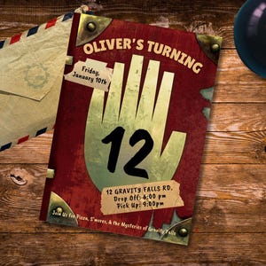 Könnte beinhalten: Eine Geburtstagseinladung mit rotem und goldenem Design, mit dem Text "OLIVER'S TURNING 12". Enthält Eventdetails und eine stilisierte Handgrafik. Ein Umschlag und eine Billardkugel mit der Nummer acht sind ebenfalls zu sehen.