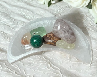 May include: A white selenite crescent moon bowl with a variety of crystals inside, including green aventurine, pink rose quartz, green malachite, and a brown and white crystal.