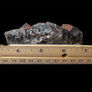 May include: A cluster of dark purple amethyst crystals with a reddish-brown matrix. The crystals are approximately 5 inches long and are measured against a wooden ruler.