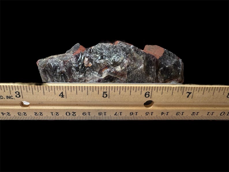May include: A cluster of dark purple amethyst crystals with a reddish-brown matrix. The crystals are approximately 5 inches long and are measured against a wooden ruler.