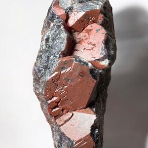 May include: A large, rough, dark gray and red crystal cluster. The crystal has a pointed shape and is composed of many smaller crystals.