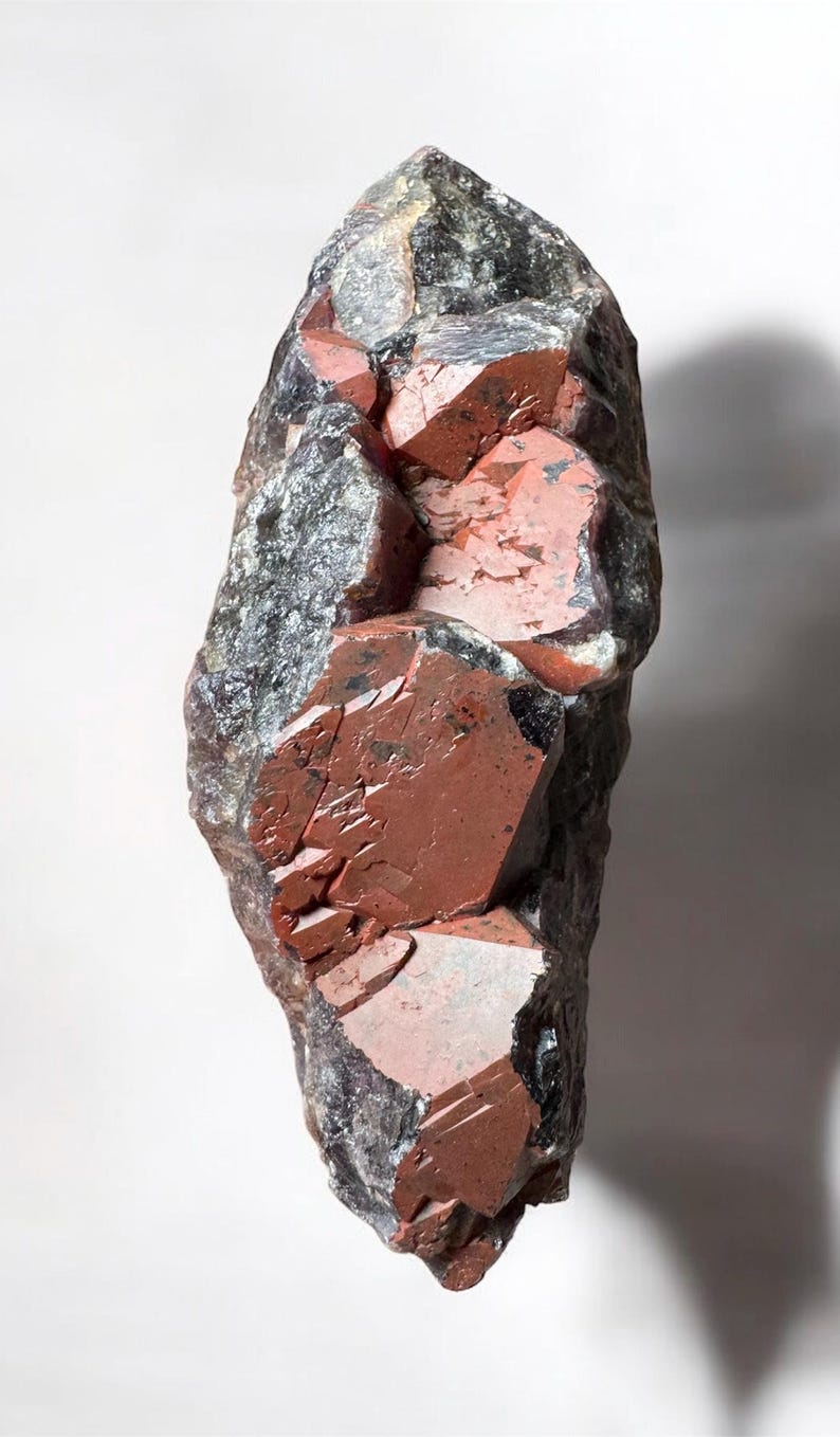 May include: A large, rough, dark gray and red crystal cluster. The crystal has a pointed shape and is composed of many smaller crystals.