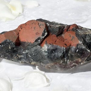 May include: A large, dark gray and red crystal cluster with a rough, natural texture. The crystal is translucent and has a variety of shapes and sizes.