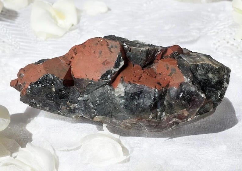 May include: A large, dark gray and red crystal cluster with a rough, natural texture. The crystal is translucent and has a variety of shapes and sizes.