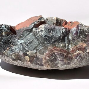 May include: A large, irregularly shaped amethyst geode with a deep purple and green color. The geode has a rough, natural surface and is filled with crystals.
