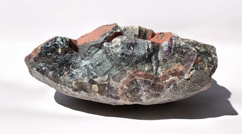 May include: A large, irregularly shaped amethyst geode with a deep purple and green color. The geode has a rough, natural surface and is filled with crystals.